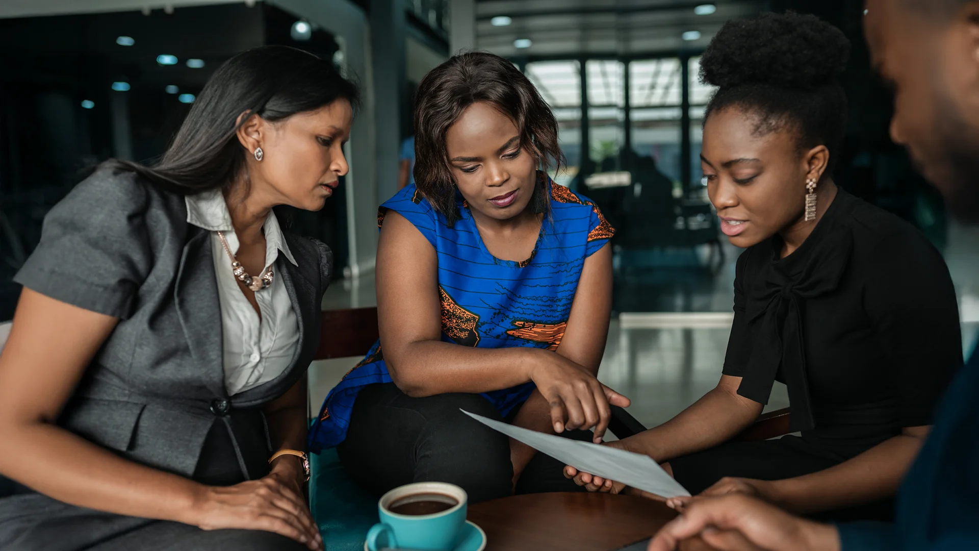 Professional Women Collaborating Over Documents In Modern Office Setting Group of diverse businesswomen reviewing a document together during a meeting in a contemporary office space.